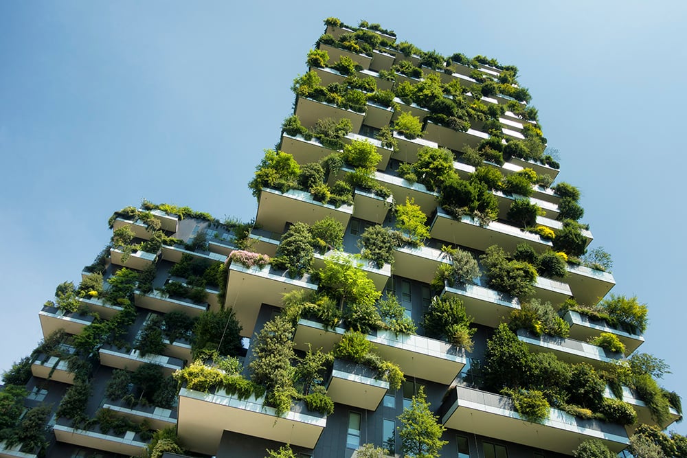 A tall apartment block with lots of greenery hanging from the balconies