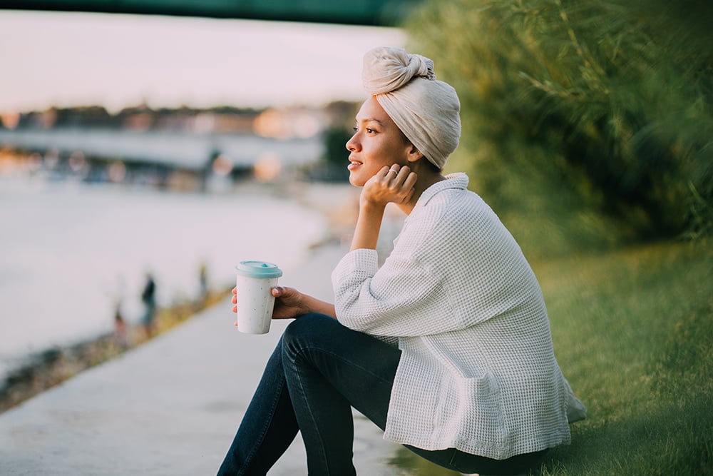 A woman looks over a river holding a reusable coffee cup