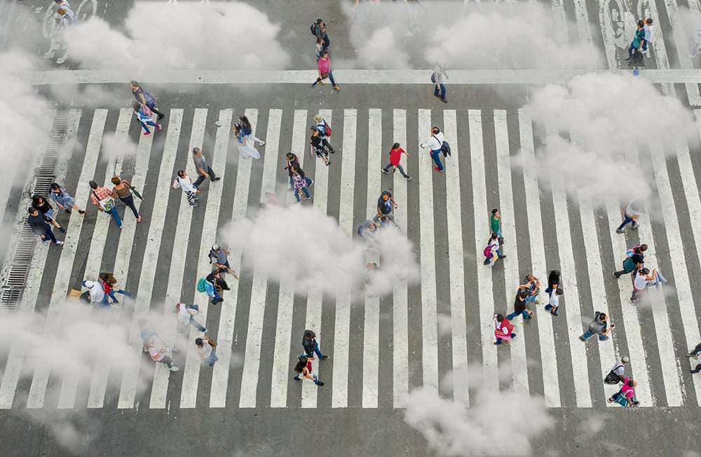 People walk across a busy zebra crossing, representing a busy city