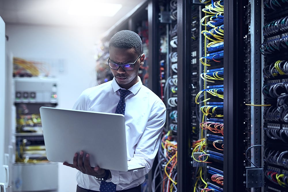 A man works on a laptop in a server room